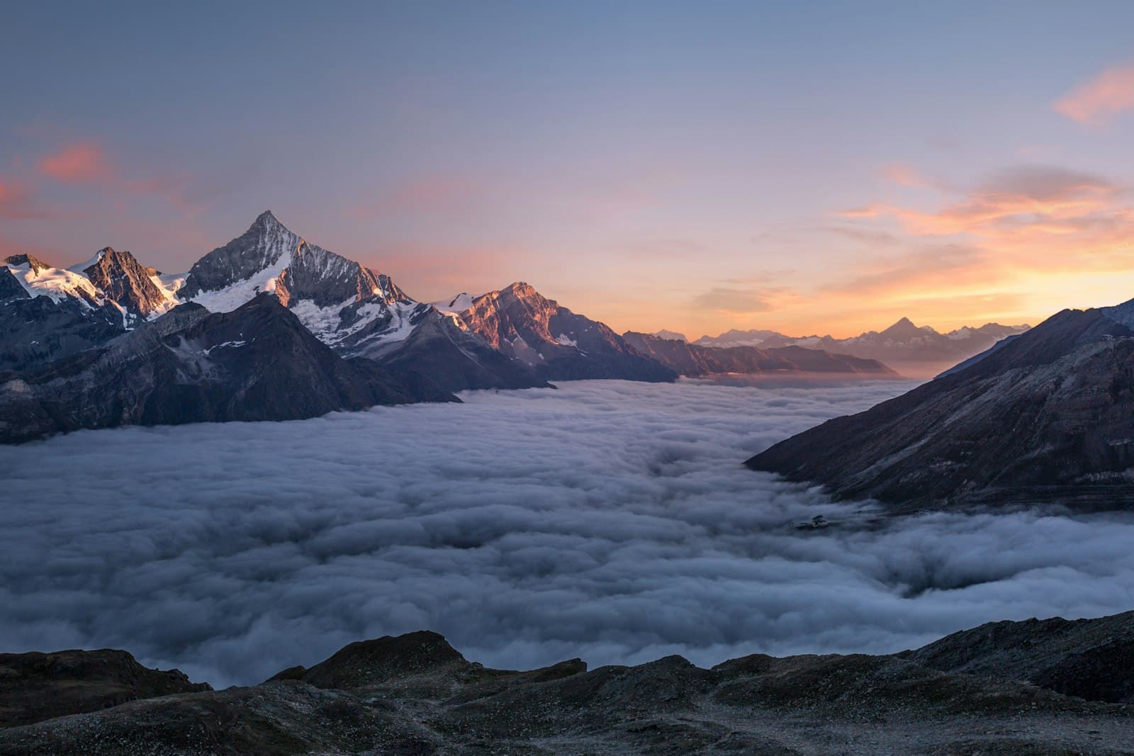 A snow-dusted peak rising above a soft sea of cloud at sunrise